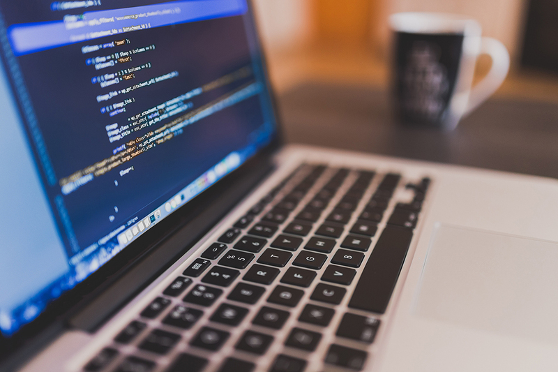 laptop computer displaying lines of programming code, with a blurred coffee cup in background